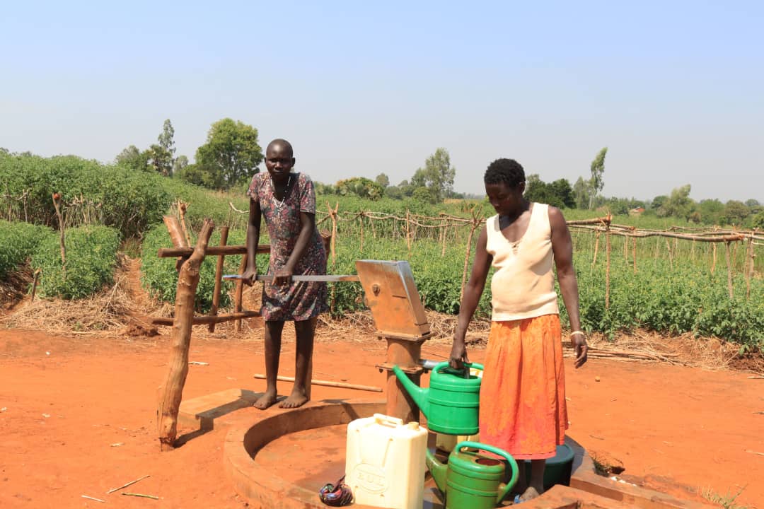 two people fill water containers at a water tap in Uganda