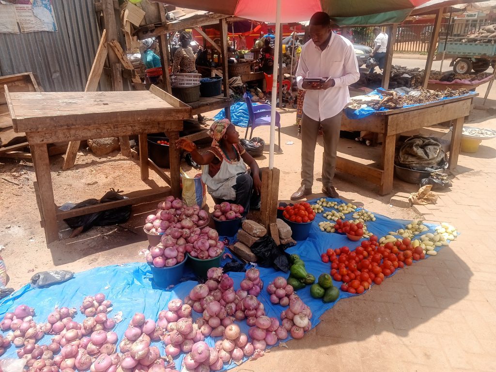 Nana Asare talks to a vegetable seller sitting with vegetable in the market
