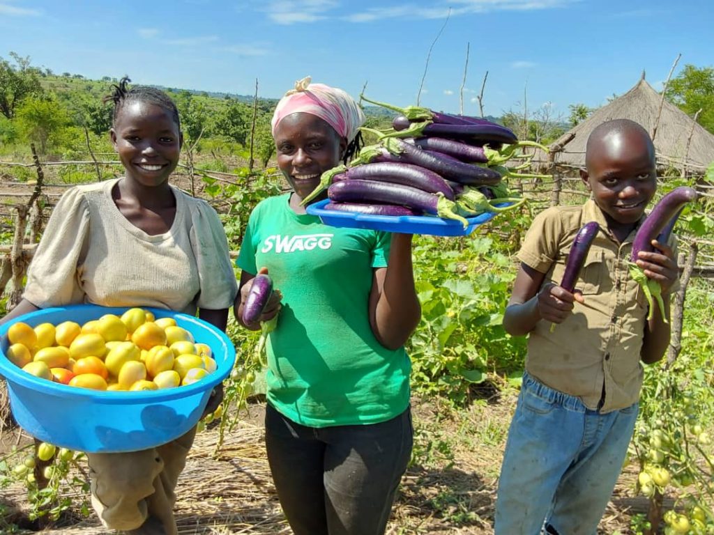 Doreen Biyiga and her children hold vegetables in her kitchen garden
