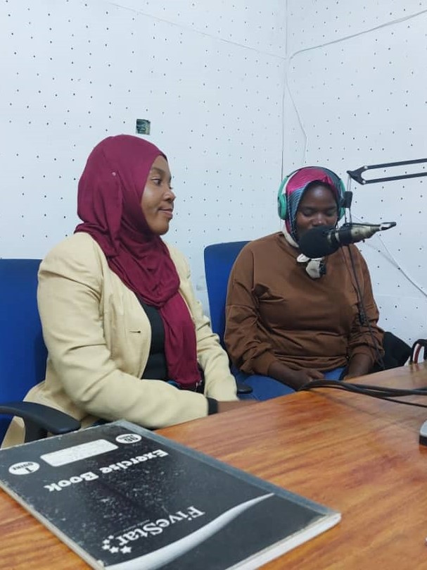 EWS-KT Technical Field Officers Hadija Lihumbo and Lydia Mkopa sit in front of microphones at the radio station.