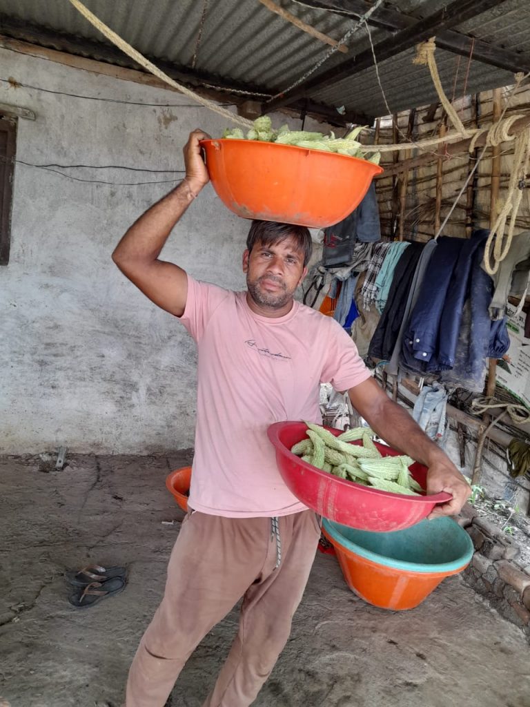 Sanjay Patidar holds a large container of bitter gourd fruit in one hand and another container on his head.