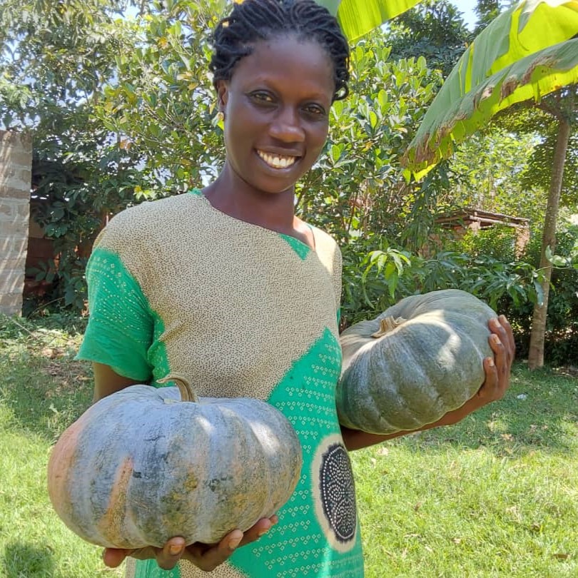 Farmer Cynthia Anyago smiles while holding two pumpkins