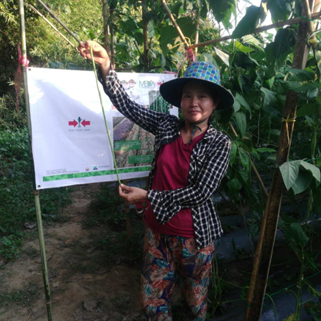 Farmer Daw Naw Eae Tho stands in front of the sign for her demo plot
