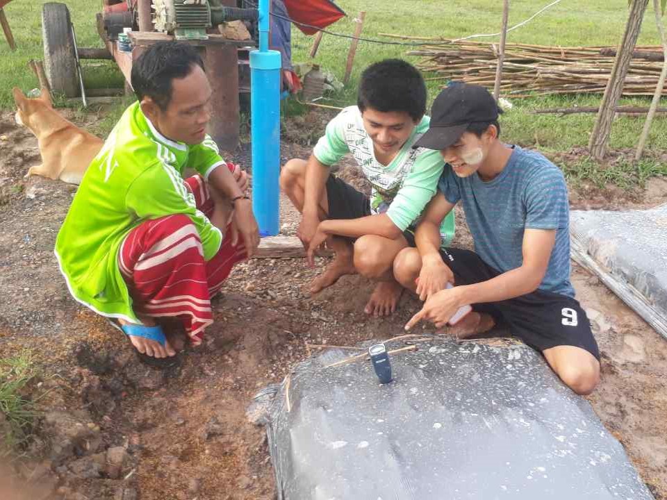 Three people measuring the pH of soil in a raised bed.