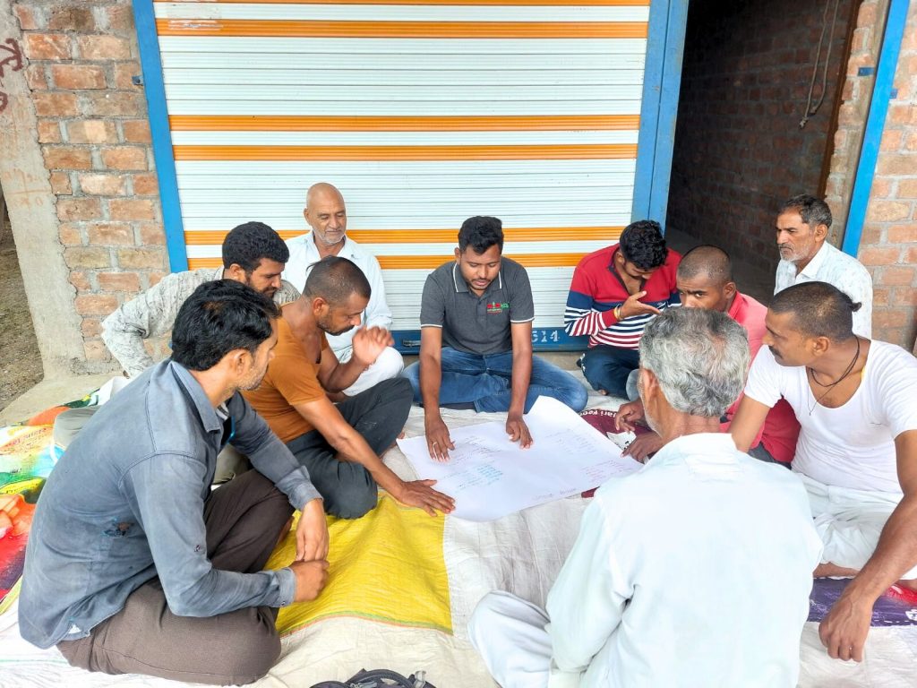 An EWS-KT trainer in India explains business planning to a group of seated farmers.