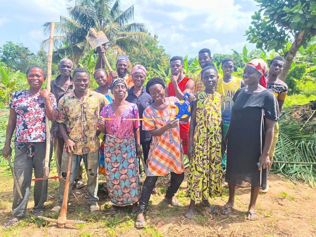 Smiling male and female farmers pose with farm tools after preparing the land and establishing a raised bed.