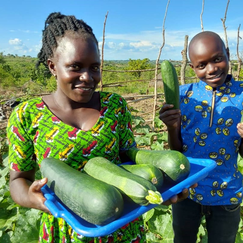 Doreen Biyiga and one of her children hold up harvested vegetables in her kitchen garden