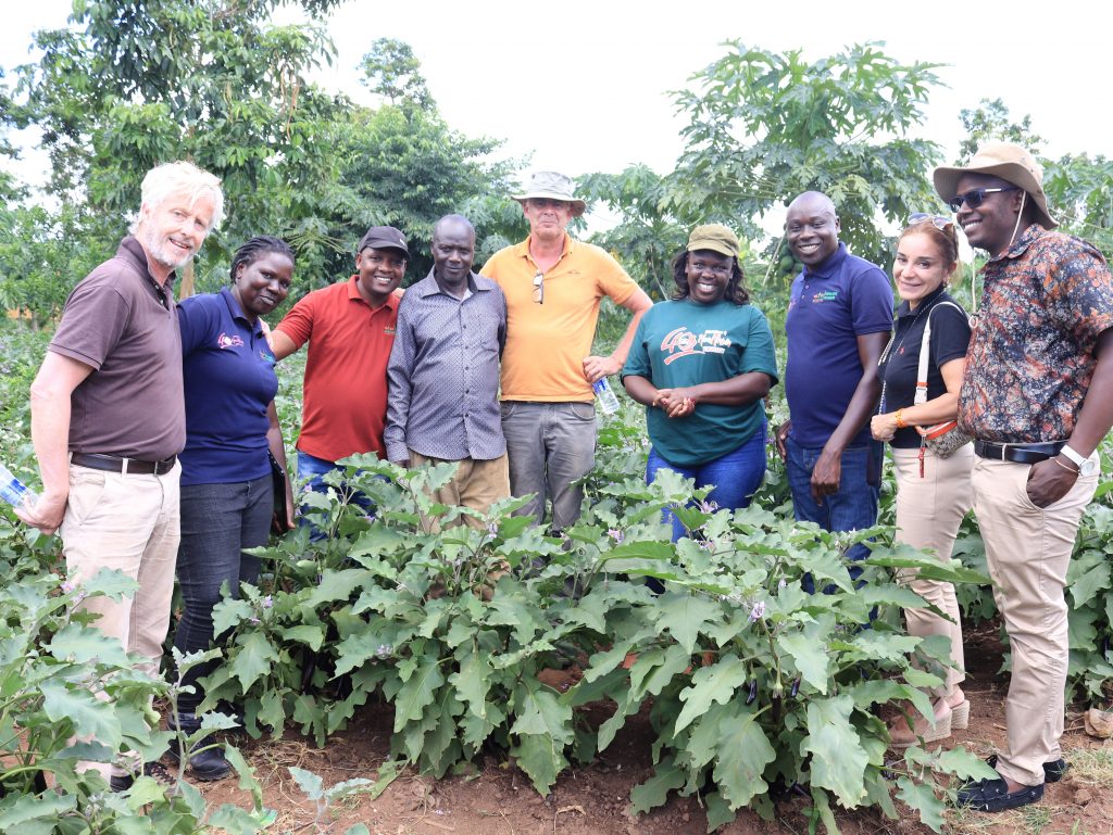 EWS-KT and SFSA leaders and other visitors stand with a farmer in his field in Uganda.