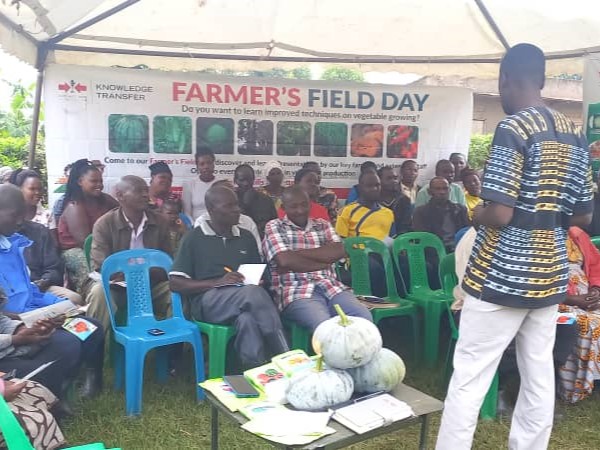 Group of farmers seated in front of Field Day banner, with pumpkins stacked in the foreground.