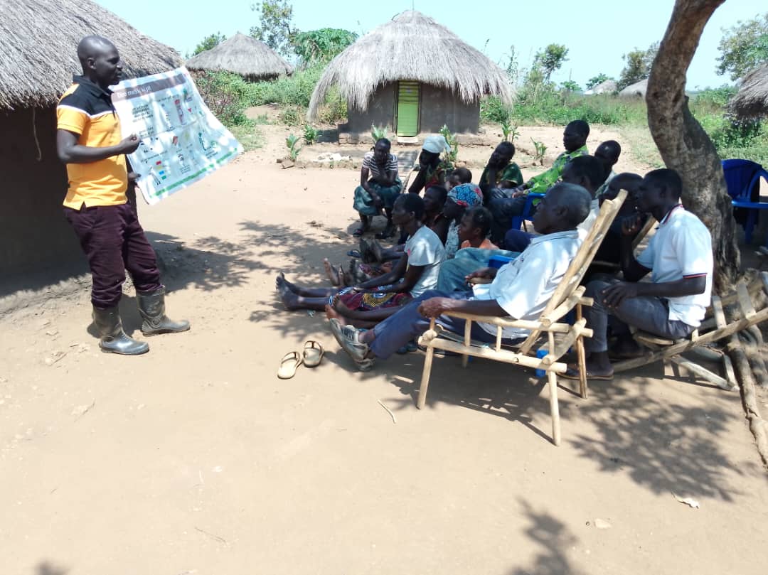 Technical Field Officer holds up training banner in front of seated farmers.
