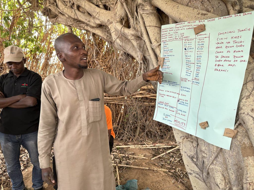 Farmer Biliyaminu Liman discusses his farm business plan, which is tacked to a tree.