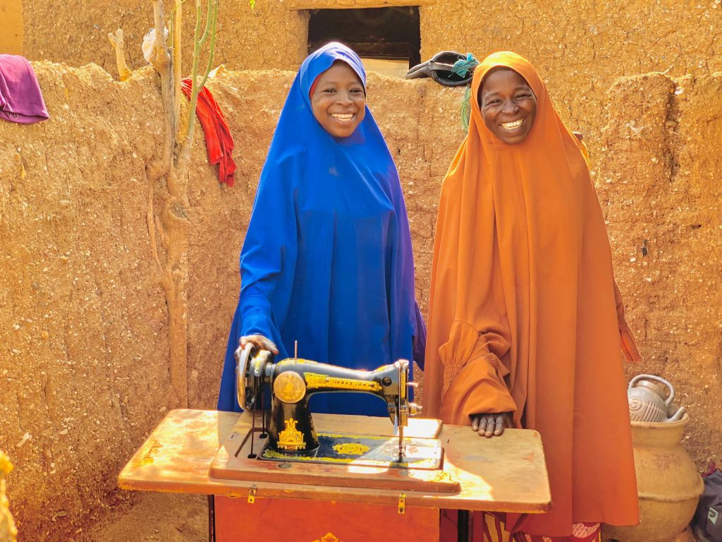 Uwandiya Alhaji and her daughter stand behind a new sewing machine on a table.