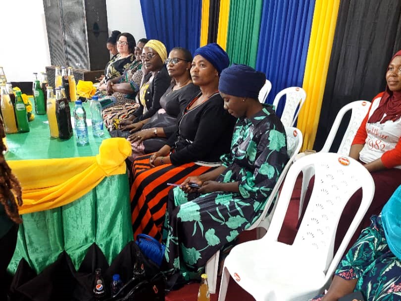 Technical Field Officer Hadija Muhidini waits with the other presenters in chairs at the front of the room.
