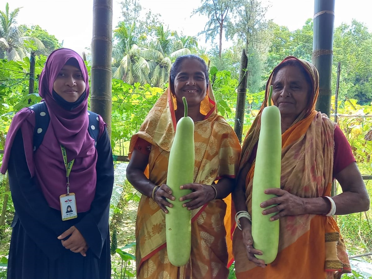 EWS-KT staff and two women farmers holding large vegetables.