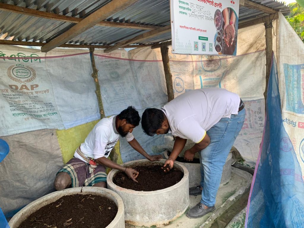 Male ESW-KT staff member and male farmer inspect the farmer's vermicompost operation.