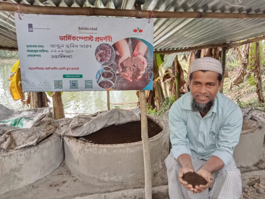 Farmer Abdul Jalil Akon holds a handful of vermicompost in front of the concrete rings that hold his vermicompost operation.