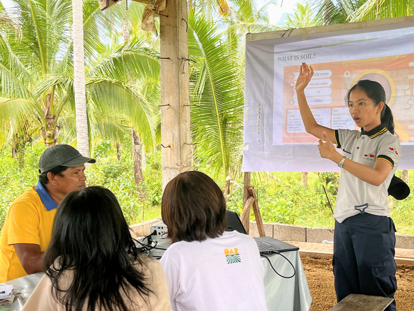 EWS-KT staff gestures as she explains about soil health to assembled farmers.