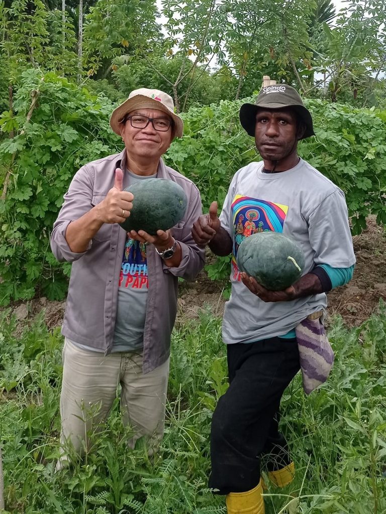 YBTS Extension Manager Edwin Saragih and farmer Marthen Luther stand in a filed while holding melons.