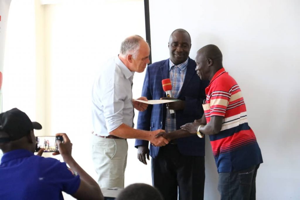 EWS-KT Executive Director Stuart Morris and Lira District Production and Marketing Officer Thomas Okello present a certificate to Alex, a male farmer.