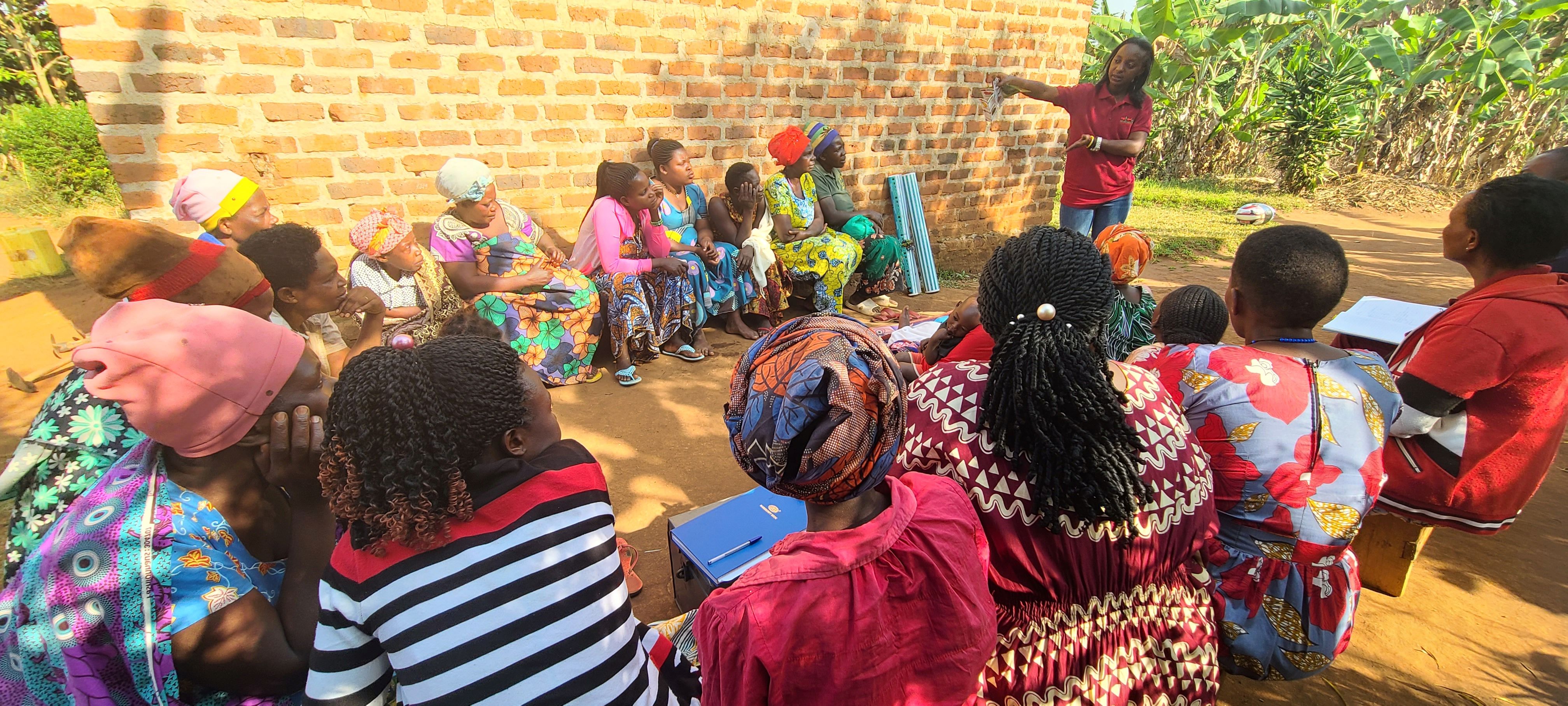EWS-KT Technical Field Officer Faith Akampumuza speaks to a group of seated farmers.