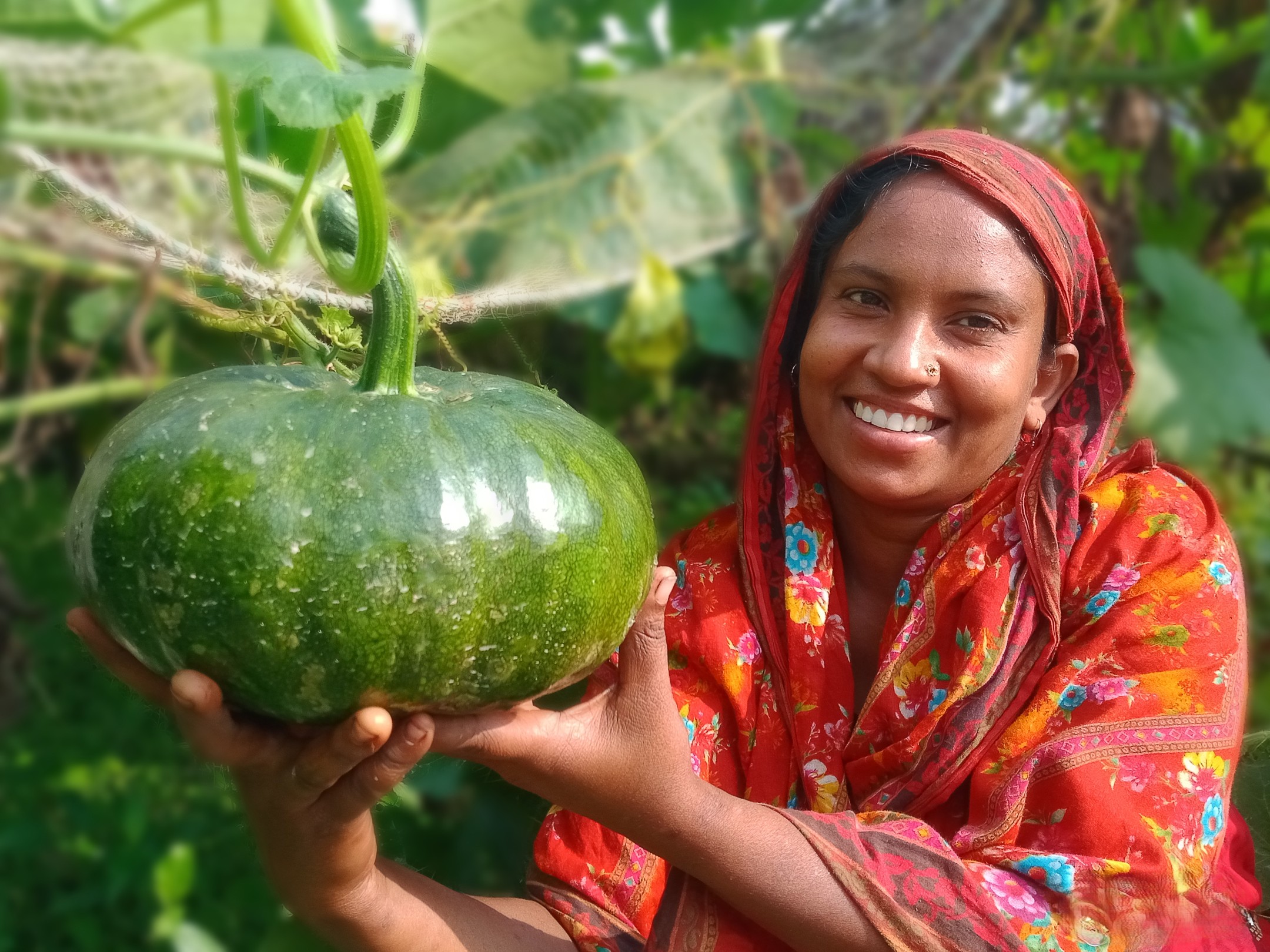 Farmer Asma Akter smiles as she shows off one of her growing pumpkins.