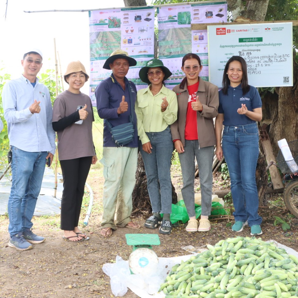 Farmers and trainers with training posters in the background and harvested cucumbers in the foreground.