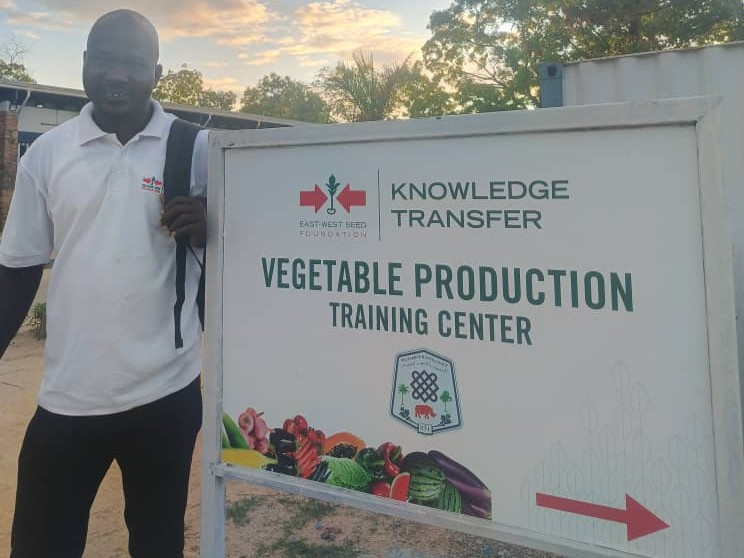 A man stands next to the sign leading to the learning farm, or vegetable production center, at the University of Juba, South Sudan.