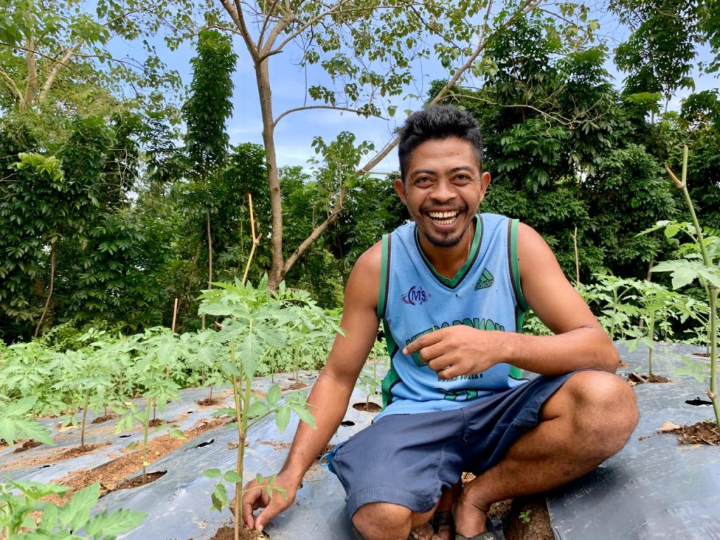 Male farmer smiles broadly between rows of healthy plants.