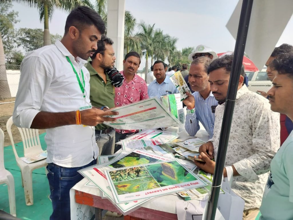 EWS-KT staff member holds up a large flashcard about bacterial wilt while talking to visitors to the booth. On the table, other flashcards help visitors to identify the root causes of common plant issues.