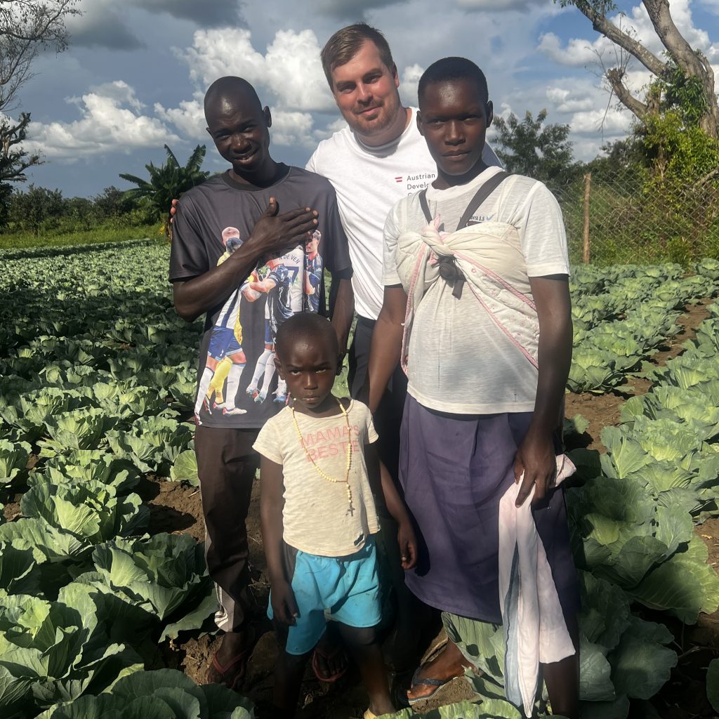 Maximilian Zangl, of Austrian Development Agency, stands with farmer Santos and his wife and child in their cabbage field.