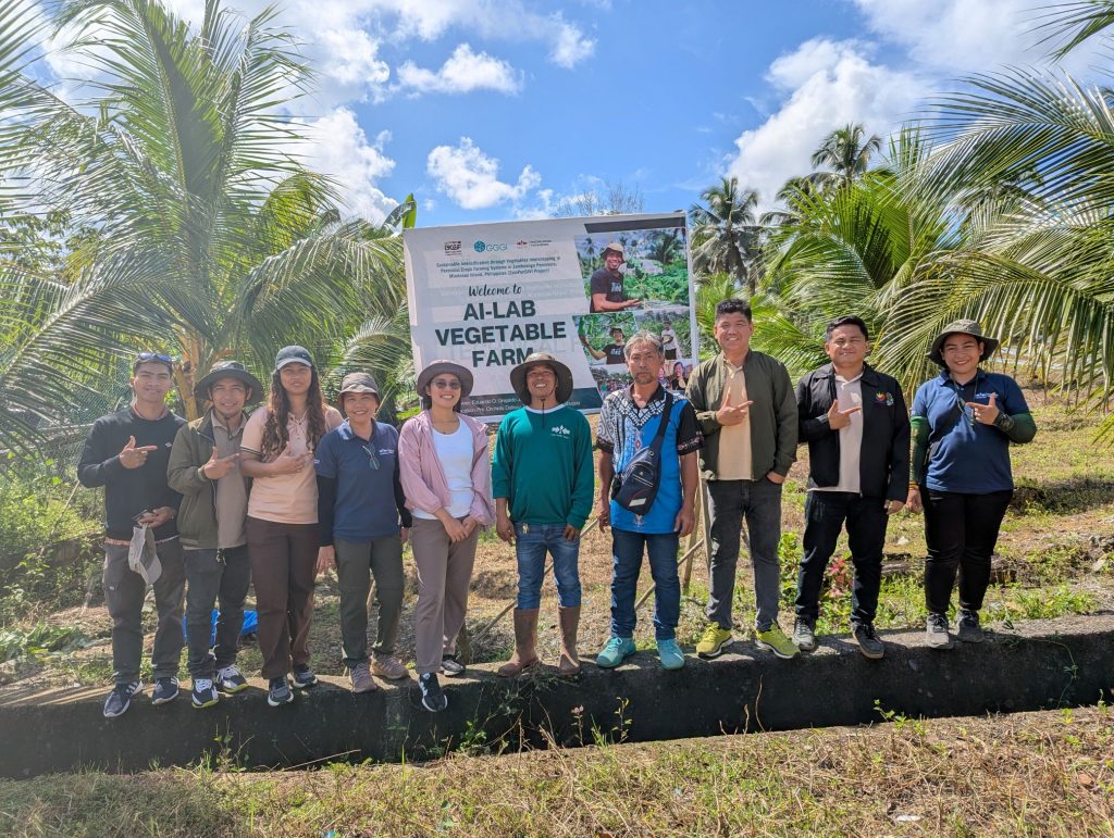 The banner for Ai-Lab Vegetable Farm behind a row of people.