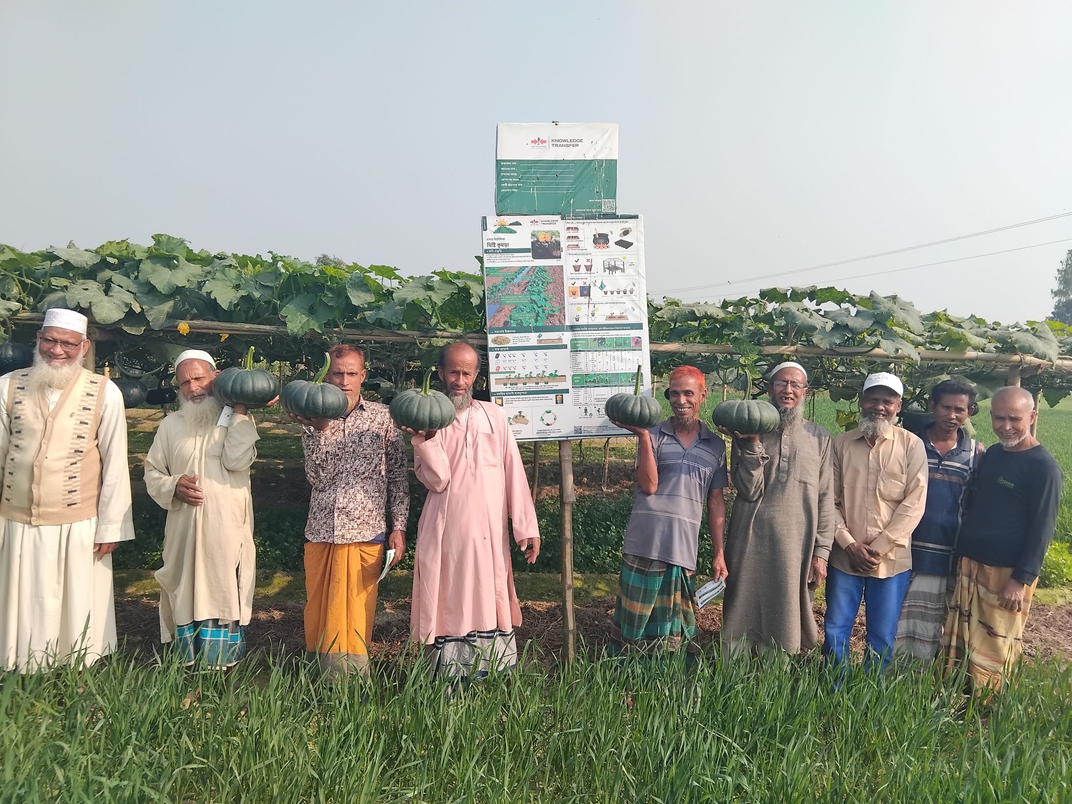 Male farmers hold pumpkins in front of a pumpkin demonstration field.