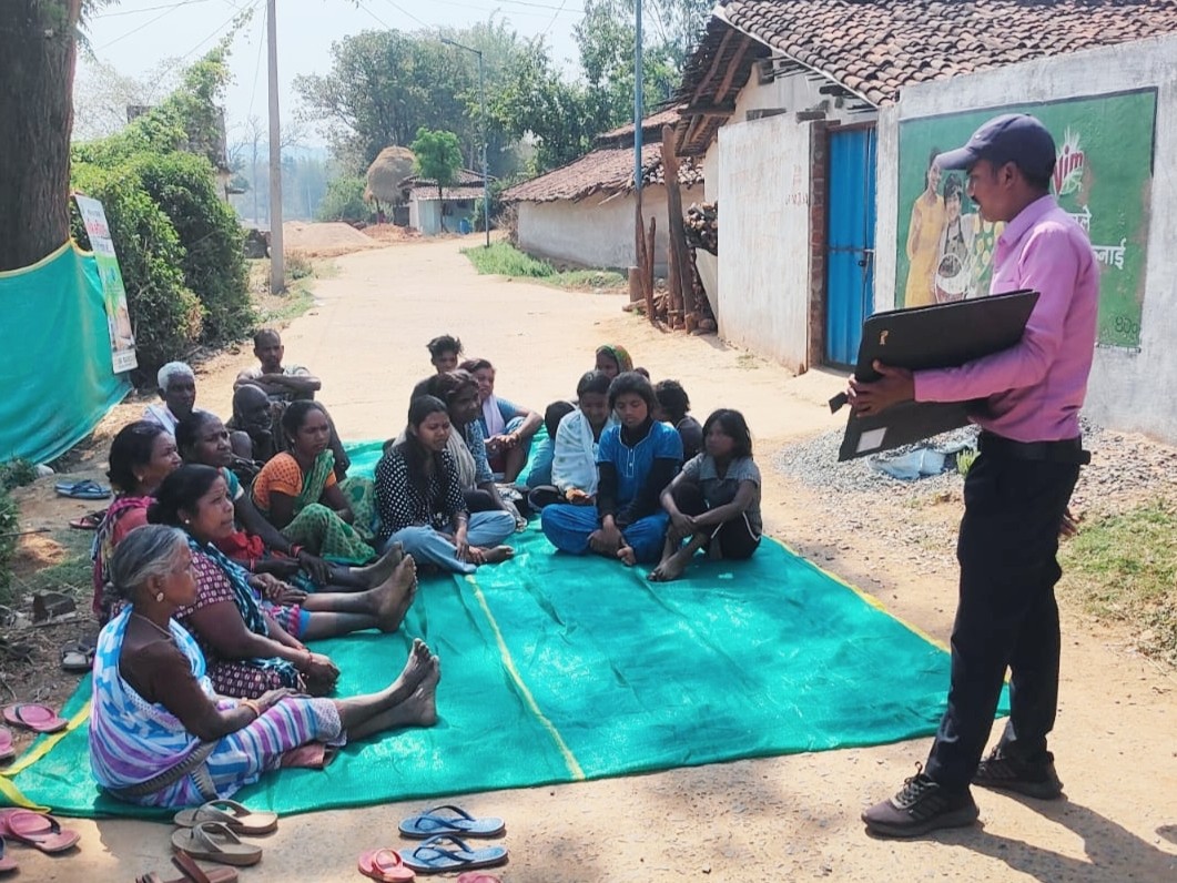 Farmers and community members sit on the ground as they learn about EWS-KT and share their farming challenges with the EWS-KT Technical Field Officer.