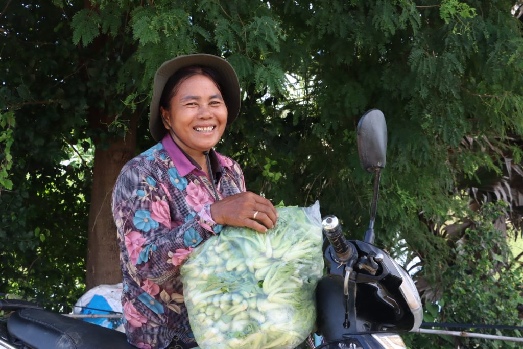 Cambodian farmer and vegetable collector Orn Somaly rests a clear bag of leafy greens on her motorbike.