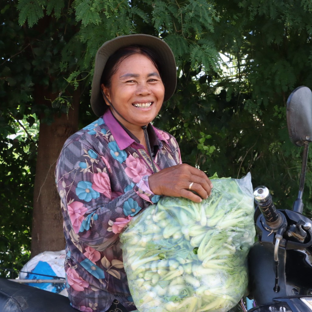 Cambodian farmer and vegetable collector Orn Somaly rests a clear bag of leafy greens on her motorbike.